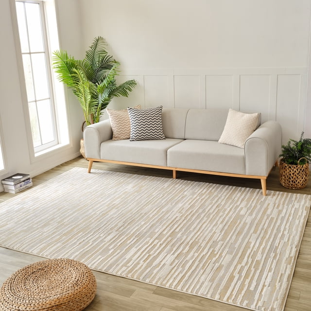 Beige brown Rug Branch Nomad abstract indoor area rug under a modern light gray sofa with chevron pillows in bright living room featuring plants and wood flooring.