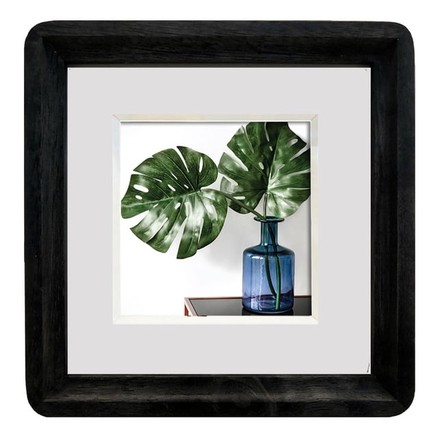 Hometrends Curved Edge 6x6in Wood Photo Frame Black with rounded edges and a thick white mat holding a 4x4 inch photo of two green monstera leaves in a blue glass vase on a reflective surface, suitable for wall hanging or tabletop display in home décor and ideal for small artwork.