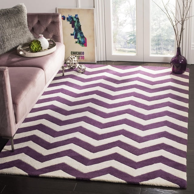 Safavieh Chatham Jake Zigzag Stripes Area Rug with purple and white zigzag stripes, hand-tufted wool with medium pile for softness, placed on dark hardwood floor in a contemporary living room featuring a mauve velvet tufted sofa, decorative tray with succulent and vase, framed Chicago map art, and a purple vase with branches near glass doors. The durable striped rug is also suitable for adding a modern accent to office or study spaces.