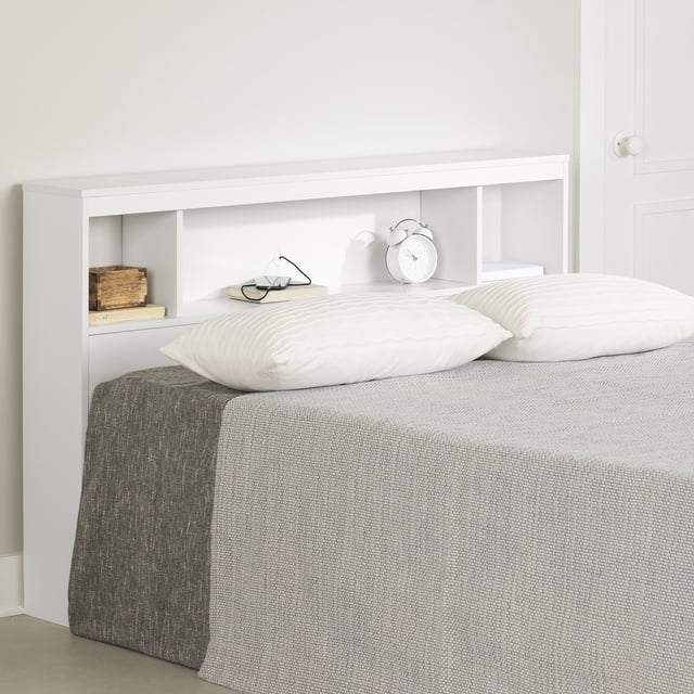 South Shore Fusion Full Bookcase Headboard in pure white with three open storage compartments holding books, glasses, and a white alarm clock, paired with a bed dressed in grey and white bedding and pillows, suitable for bedroom storage and decor organization.