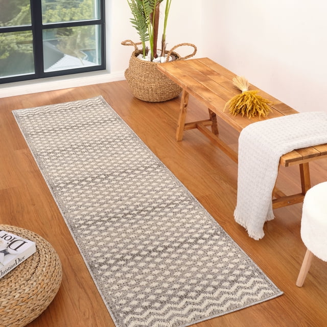 Rug Branch Jules Moroccan Indoor Area Rug, Grey Beige, Geometric - a grey and beige polypropylene runner rug with a geometric diamond and zigzag pattern and 0.3-inch pile height, placed on a hardwood floor beside a wooden bench with a light grey throw and dried yellow flowers, near a woven basket planter with green plants and a round woven ottoman holding a book, suitable for high-traffic indoor areas like hallways and kitchens.