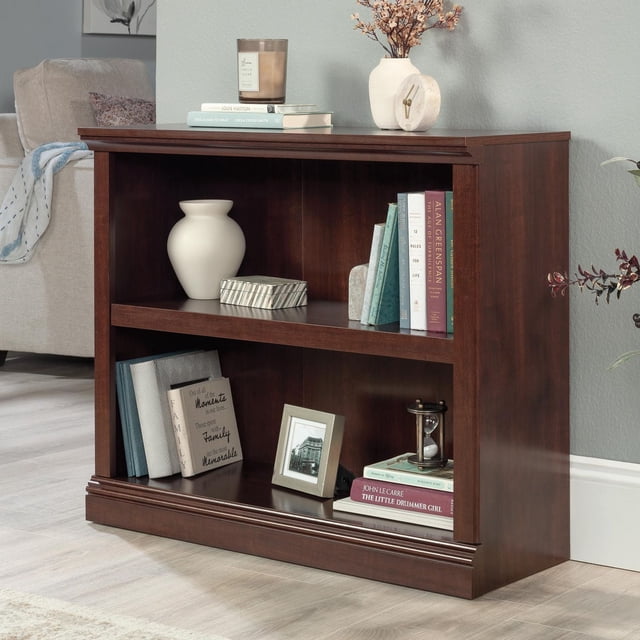 Sauder Select Bibliothèque à 2 Tablettes en Fini Bois Foncé avec Deux Tablettes Spacieuses, Incluant une Tablette Ajustable, Tenant des Livres, un vase Blanc, une Boîte Décorative, une photo Encadrée, un Sablier et une Petite Horloge, Posée sur un Plancher de Bois Clair contre un Mur Bleu Pâle Près d'Un sofa beige, Idéale pour le Rangement Multi-Pièces au Bureau Ou dans les Aires de Vie.