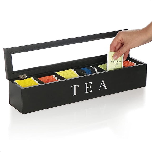 Tea Support pour Sachets de Thé à 6 Compartiments, une Boîte à Thé en Bois avec une Finition Noire Élégante et le Mot « » Imprimé à l'Avant. la Boîte Présente un Couvercle à Charnière et six Compartiments pour Organiser Soigneusement des Sachets de Thé Colorés. une Main Est Montrée Plaçant un Sachet de Thé dans l'Un des Compartiments. Convient pour Organiser des Sachets de Sucre, des Édulcorants Ou de Petites Fournitures de Bureau.