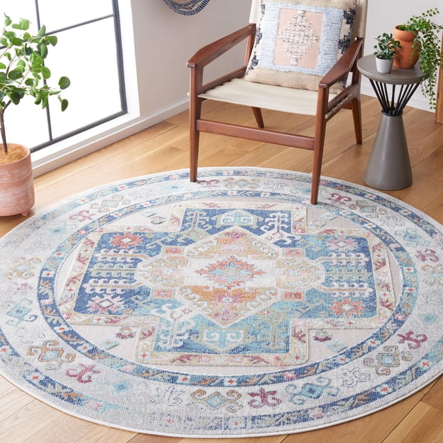 SAFAVIEH Cabana Dima Medallion Indoor/Outdoor Area Rug, round with a tropical medallion pattern in blue, beige, and pastel shades, crafted from durable synthetic yarns resistant to weather and fading, displayed on a light hardwood floor next to a wooden armchair with a textured cushion and two potted plants, ideal for busy indoor or outdoor areas.