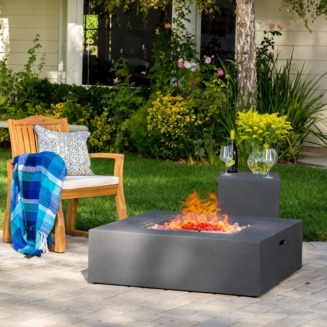Alar Table de Foyer au Gaz Extérieur Carré Gris Foncé 50K BTU avec Support de Réservoir. Ce Foyer, Fabriqué à Partir d'Oxyde de Magnésium, Présente un design Moderne Gris Foncé Carré et Comprend un Support de Réservoir Assorti pour le Stockage de propane. Il Offre 50 000 BTU de Chaleur et Est Exposé dans une Cour Arrière Paysagère avec Mobilier de patio, une Couverture et des Plantes Décoratives. Dimensions : Foyer - 39,91 Po P x 39,91 Po L x 12,40 Po H; Support de Réservoir - 13,78 Po P x 15,75