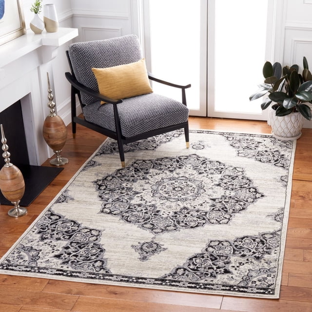 SAFAVIEH Brentwood Dimitri Floral Bordered Area Rug with a central medallion and floral geometric patterns in black and grey on cream, placed on hardwood flooring beside a black wooden armchair with grey upholstery and a mustard yellow pillow, near a white fireplace and a potted plant by a glass door, ideal for traditional or transitional decor.