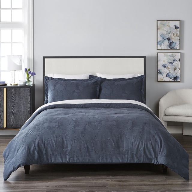 Ensemble de Douillette HT Ginko dans une Vue avant Centrée sur un Lit avec une Tête de Lit Noire et beige, Comprenant une Douillette jacquard en Coton/polyester Sarcelle et des Couvre-Oreillers Assortis avec des Motifs Botaniques Brodés, dans une Chambre Moderne avec un Plancher de Bois, une Table de Nuit Noire avec accents Dorés, une Lampe Blanche, des Fleurs Violettes et Deux Peintures Florales sur un Mur Gris Pâle. l'Ensemble Convient Aussi pour Ajouter une Touche Botanique Apaisante aux Chambres d'Amis.
