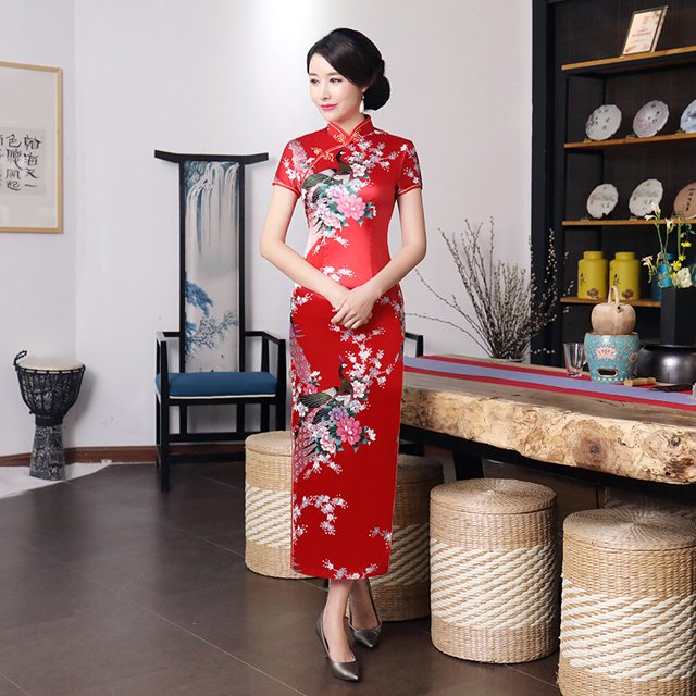 Robe Qipao Longue pour Femmes Multicolore Rétro Classique Style Chinois Imprimée Qipao Grande Taille Coupe Ajustée. Cette Élégante Robe Rouge Présente des Motifs Floraux, un Col mandarin et une Coupe Ajustée, Idéale pour les Robes Décontractées Ou la Mode pour Femmes. Parfaite pour les Événements Formels, les Mariages Ou les Rassemblements Décontractés. Exposée dans un Cadre de Pièce Traditionnel avec des Tabourets Tressés et des Éléments Décoratifs.