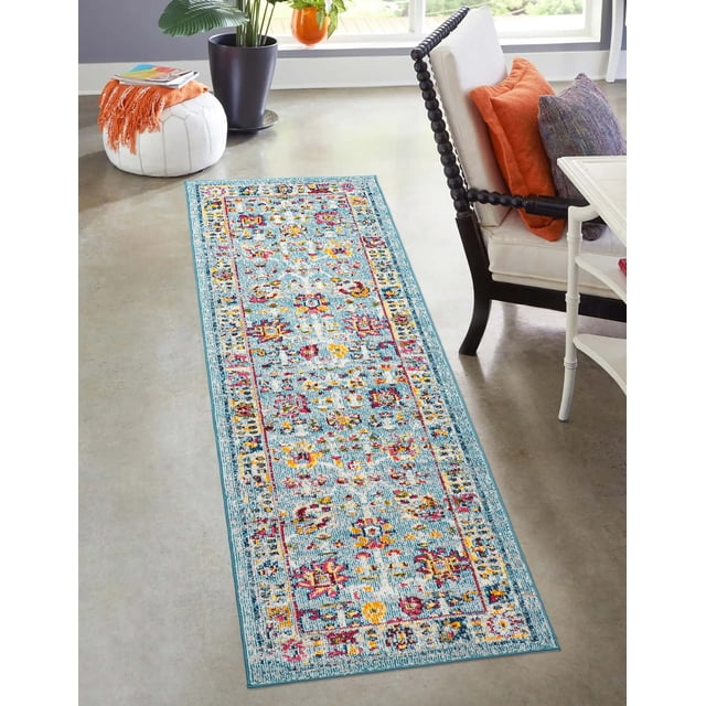ECARPET Aldora Traditional Area Rug for Living Room, Bedroom, Dining Room, Entrance, Hallway and More with a vintage-inspired floral pattern in blue, red, yellow, and white. This rectangular accent rug lies on a polished concrete floor beside a white cushioned chair with orange and gray pillows, a white side table, and a white pouf with an orange throw, adding warmth and texture to modern interiors.