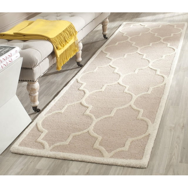 Safavieh Cambridge Kevin Geometric Area Rug in light beige wool with a raised cream geometric pattern, hand-tufted with plush cut piles, placed on a light wood floor beside a beige upholstered bench with wooden legs and a yellow throw blanket, suitable for adding texture and warmth to hallways or entryways.