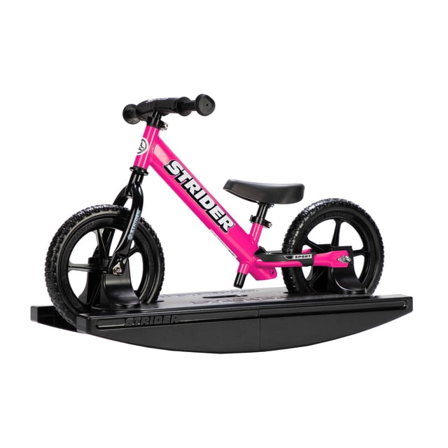 Strider - 12 Sport 2-in-1 Rocking Bike in pink, designed for children aged 6 months to 5 years. The bike is shown mounted on a black rocking base, which securely holds it in place for stationary play. The lightweight frame features toddler-sized grips, a cushioned seat, and no-tool adjustable handlebars and seatpost. The black tires are puncture-proof, and the bike is suitable for teaching balance and coordination. Ideal for transitioning from rocking to riding.