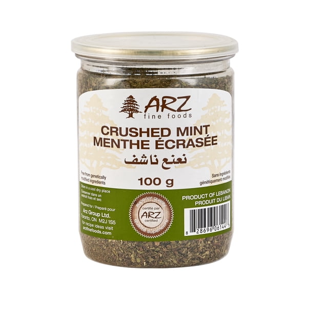 Arz Mint Crushed 100g in a clear plastic jar with a beige lid, containing crushed dried mint used as a Middle Eastern spice and seasoning. The label shows the ARZ fine foods logo with a cedar tree, product name in English, French, and Arabic, storage instructions to keep in a cool dry place, and certification. Marked as a product of Lebanon with a barcode.