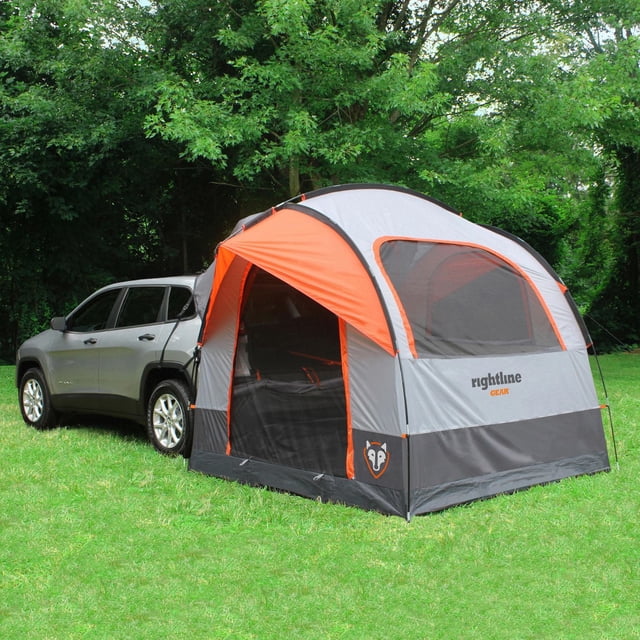 Rightline Gear SUV Tent in grey and orange attached to the back of a silver SUV on grass with trees behind, featuring large mesh windows, a dome shape, and black bottom panel, ideal for camping and truck tent use.
