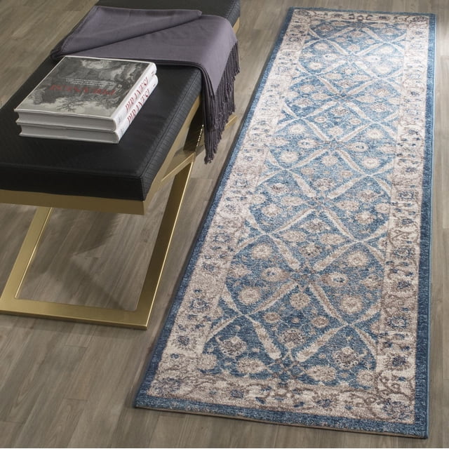 Safavieh Sofia Tapis Coureur à Bordure Florale Jerrod avec motifs Floraux Traditionnels dans des Tons Bleu et beige Usés, Posé sur un Plancher de Bois à Côté d'Un Banc Matelassé Noir avec Pattes Dorées, Drapé avec un Jeté Gris Foncé et des Livres Empilés.