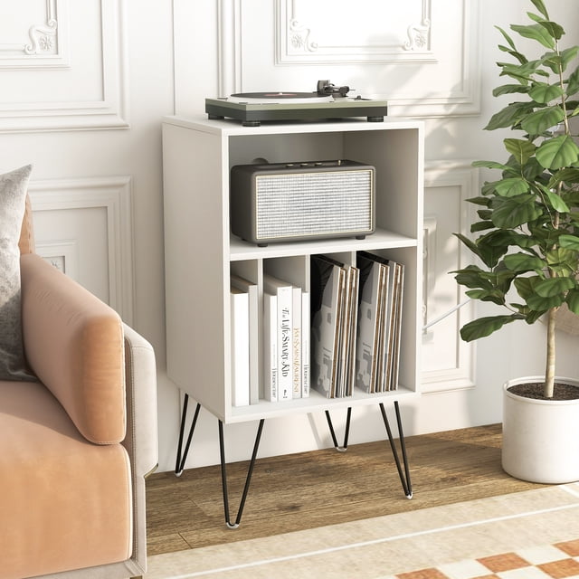 Giantex Support pour Tourne-Disque en Blanc, avec un Dessus en Bois Robuste, des Pattes Métalliques Stables et une Barre d'Alimentation Intégrée avec 2 Prises, 2 ports USB et 1 port Type-C. le Support Comprend une Couche Supérieure pour un Plateau Tournant, une Tablette Ouverte pour Accessoires audio et Quatre Séparateurs pour Organiser des Disques Vinyles, des Livres Ou des CD. Présenté dans un Décor de Salon avec un Plateau Tournant, un Haut-Parleur et des Disques Vinyles Exposés, Complété par un sofa à Proximité et une Plante en Pot.