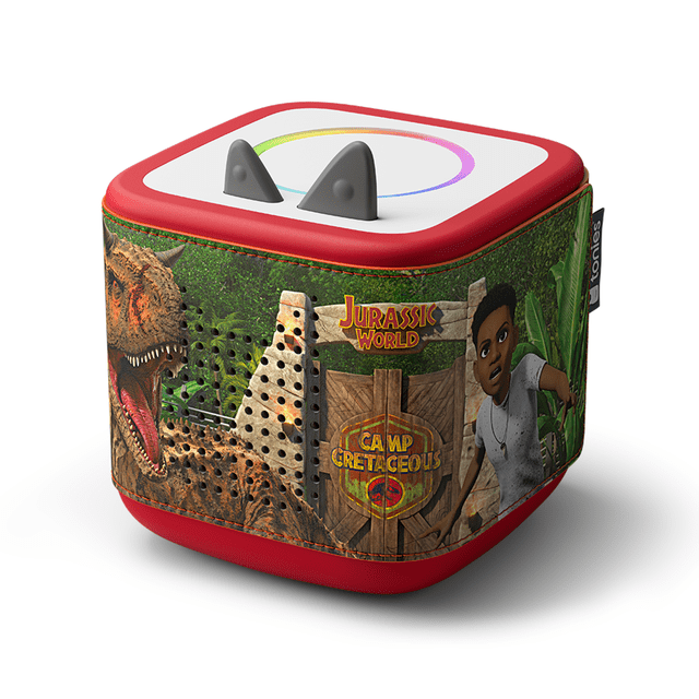 tonies Toniebox 2 Sleeve: Jurassic Park with a red silicone sleeve featuring a Jurassic World Camp Cretaceous design, including a roaring T-Rex, wooden gate logo, and a character in a jungle setting, fitting snugly on the Toniebox 2 with speaker holes for clear sound, suitable for children aged 1 and up.