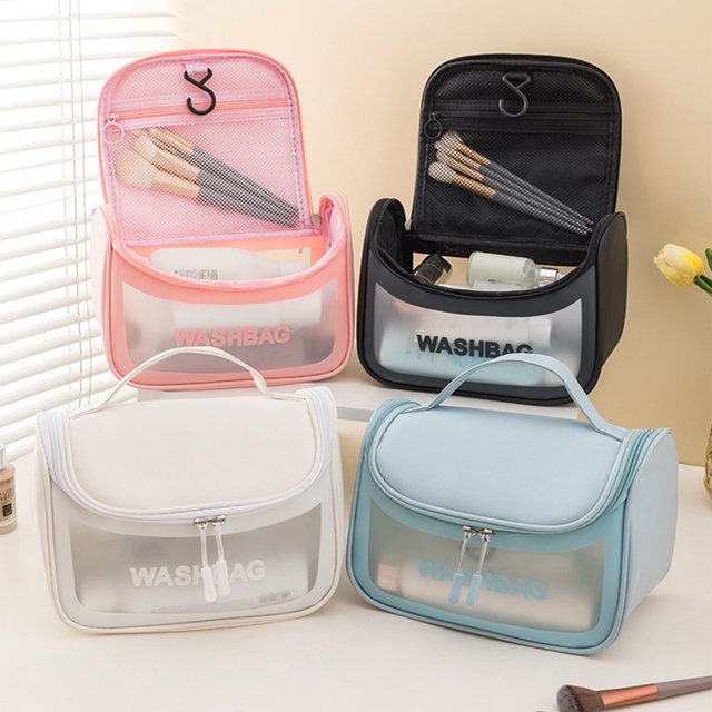 Vaidha Translucent Cosmetic Bag set with frosted translucent PVC material, zipper handles, and portable design. Includes four bags in black, pink, white, and blue colors, each featuring a flip-top compartment, mesh zippered pocket, and large main compartment for toiletries. Ideal as a travel makeup organizer, displayed upright on a table with makeup brushes and accessories nearby.