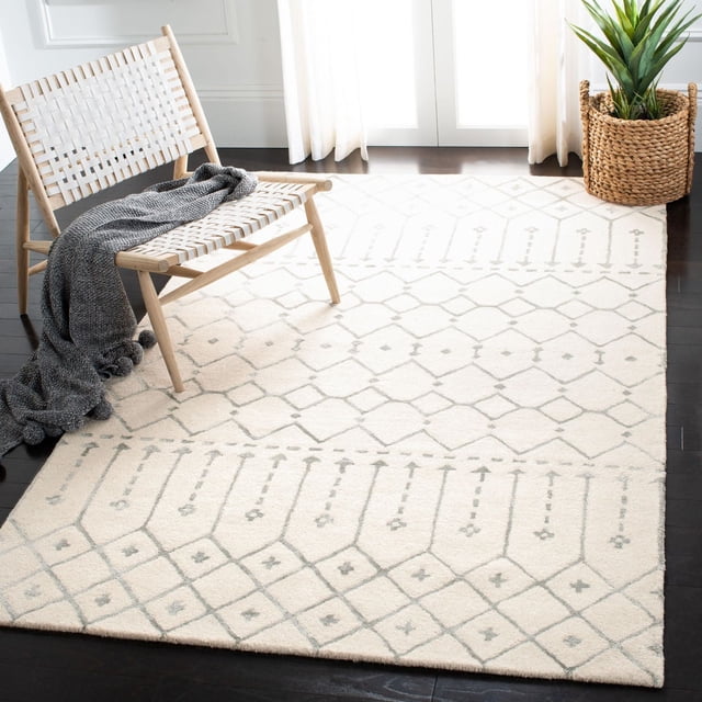Safavieh Himalaya Darin Geometric Area Rug in cream with light gray geometric patterns, made of 100 percent hand-loomed wool, shown on dark hardwood floors beneath a woven wooden chair with a gray knitted throw, next to a woven basket planter with a green plant, ideal as an accent rug for modern living spaces.