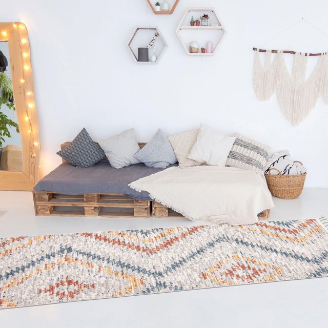 Southwestern rug from ECARPET Sun Collection featuring geometric patterns in warm tones laid on the floor of a bright living space with pallet seating and decorative wall shelves.