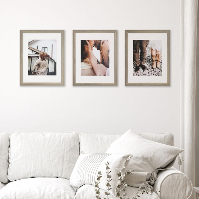 11x14 pack of 3 natural wood-look wall frames with crisp white mats and 7.5x9.5 inch photo openings, displayed on a white wall above a beige sofa with cushions and a small plant, suitable for enhancing home décor and photo display.
