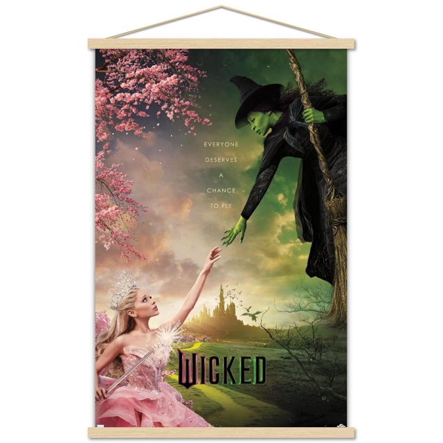 Wicked - One Sheet Wall Poster with Magnetic Frame, 22.375" x 34", depicting a green-skinned witch in a black dress and pointed hat holding a wooden broomstick, reaching down toward a princess in a sparkling pink gown and silver tiara reaching up beneath pink cherry blossom branches, with a distant castle and flying birds in the background, and the text 'Everyone deserves a chance to fly' above the title 'Wicked'.