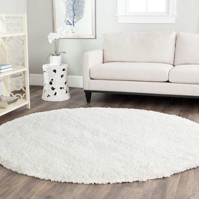 Safavieh California Solid Plush Shag Area Rug, round with a dense white polypropylene pile weighing 4.5kg per square meter, displayed on dark hardwood flooring in a living room with a beige sofa, white ceramic side table with orchid, and light wood shelving, suitable for adding plush comfort and style.