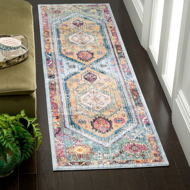 SAFAVIEH Bristol Leola Traditional Area Rug, a polyester fiber runner with a distressed antique pattern in muted blue, beige, and pink tones, placed on dark hardwood flooring beside a green sofa and potted fern, suitable for adding vintage charm to modern Canadian homes.