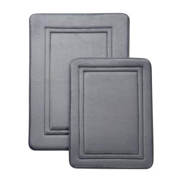 Mainstays Memory Foam Bath Mat Set in grey, featuring two cushioned rectangular mats measuring 20 by 30 inches and 17 by 24 inches, made of soft polyester with memory foam filling and non-slip backing, designed for bathroom use to provide comfort and safety when stepping out of the shower or standing at the sink.
