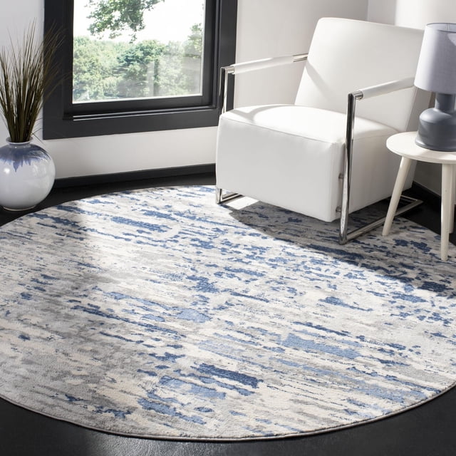 SAFAVIEH Jasper Brandt Abstract Overdyed Area Rug in a round shape with a soft cut pile featuring an abstract blue and grey pattern, placed under a white armchair with chrome arms beside a small side table and lamp near a window, suitable for enhancing contemporary decor.