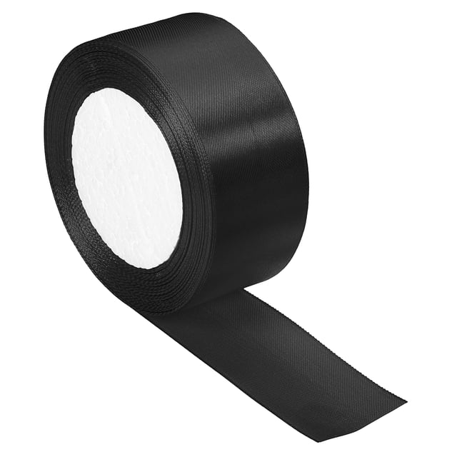 Unique Bargains 1.5 Inch Wide 24 Yards Satin Ribbon in black, made of polyester with a double-face solid design. The ribbon roll is soft to the touch, durable, and can be cut into desired lengths and shapes. Ideal for crafts, gift wrapping, flower arrangements, and DIY sewing projects. The roll measures 1.5 inches wide and 24.06 yards long, making it convenient for storage and versatile for various decorative uses.