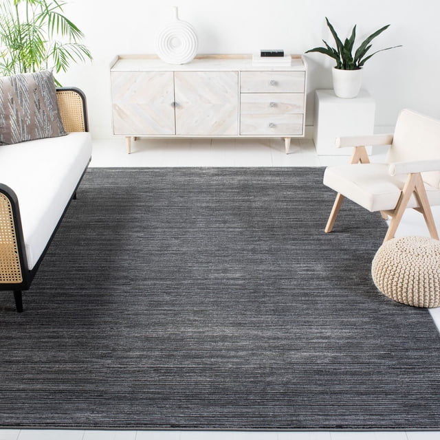 Safavieh Vision Adrasteia Overdyed Solid Area Rug in grey with subtle linear texture, placed as an accent rug in a minimalist living room with a light wood sideboard, white cushioned armchair with wooden frame, knitted pouf, and green plants, ideal for contemporary indoor spaces.