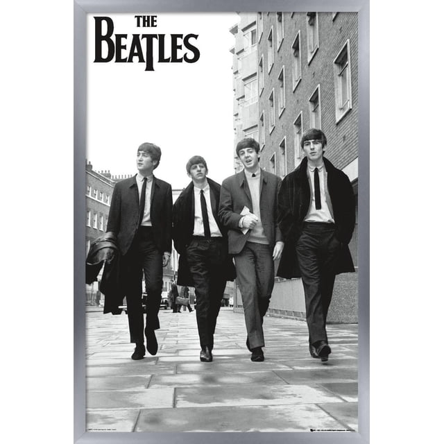 The Beatles - In London Wall Poster, 22.375" x 34" featuring a black and white photo of four men walking on a paved city street between brick buildings, dressed in 1960s suits and coats, with The Beatles logo in bold black letters at the top left, printed on glossy poster paper suitable for framing or wall mounting, often used as stylish wall art for bedrooms, offices, or dorm rooms.