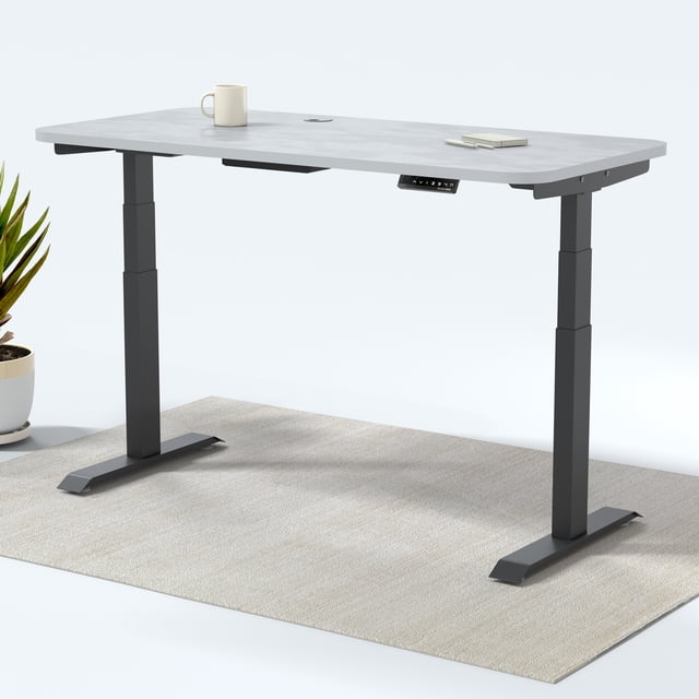 MotionGrey Bureau Assis-Debout à Double Moteur avec 4 Réglages de Mémoire, Doté d'Un Dessus Laminé Blanc de 47 Pouces par 24 Pouces et d'Un Cadre en Acier Noir. le Bureau Est Ajustable de 23,7 à 49,3 Pouces avec Deux Moteurs Allemands Bosch, Supporte jusqu'à 176 Lb. Il Comprend un Clavier à Mémoire Numérique avec 4 options de Hauteur Préréglées et un port USB Intégré. le Bureau Est Présenté dans un Cadre Minimaliste avec un Tapis beige, une Plante en Pot et une Tasse à Café en surface.