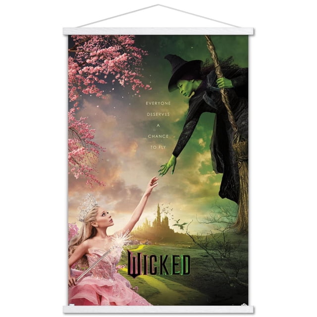 Wicked - One Sheet Wall Poster with Magnetic Frame, 22.375" x 34" depicting a green-skinned witch in black clothing holding a broomstick reaching down toward a princess in a pink gown and tiara with a sparkling wand, set against a dramatic sky with a distant castle and pink cherry blossoms, featuring the text 'Everyone deserves a chance to fly' and the title 'Wicked' at the bottom, suitable for wall art and party décor.