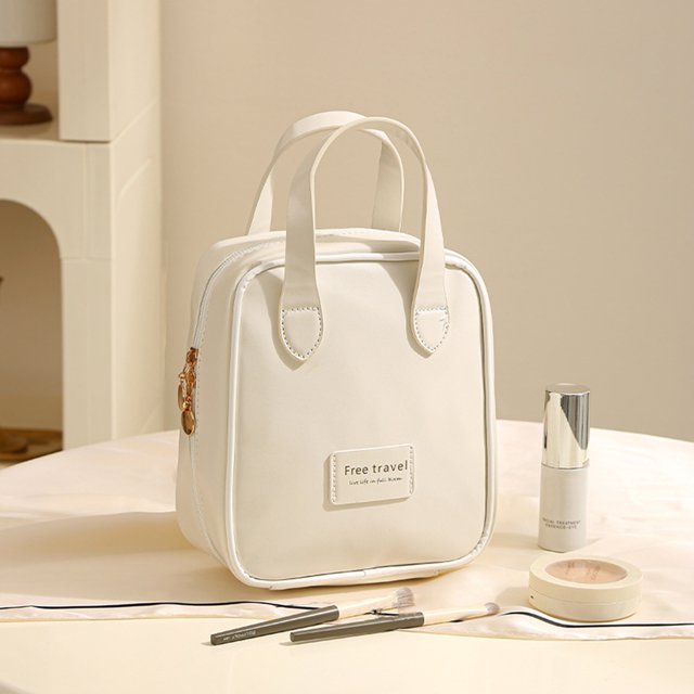 TopLLC Organization and Storage Handheld Makeup Bag with a sense of luxury and large capacity for travel. This white artificial leather bag features dual handles, a zippered closure, and a compact design. Displayed on a table with makeup items like brushes, foundation, and compact powder, it is ideal for cosmetic storage and toiletries. Perfect for travel or daily use, it combines elegance and practicality.