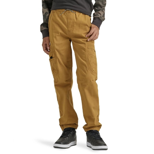 Wrangler Boy's Gamer Pant in tan brown, front view on a boy wearing black sneakers and camo long-sleeve shirt, featuring multiple cargo pockets including a large side pocket for gaming devices, elastic cuffs, pull-on jogger style with adjustable drawcord waistband, relaxed fit through seat and thigh, made from 98% cotton and 2% spandex, ideal for active boys needing functional storage.