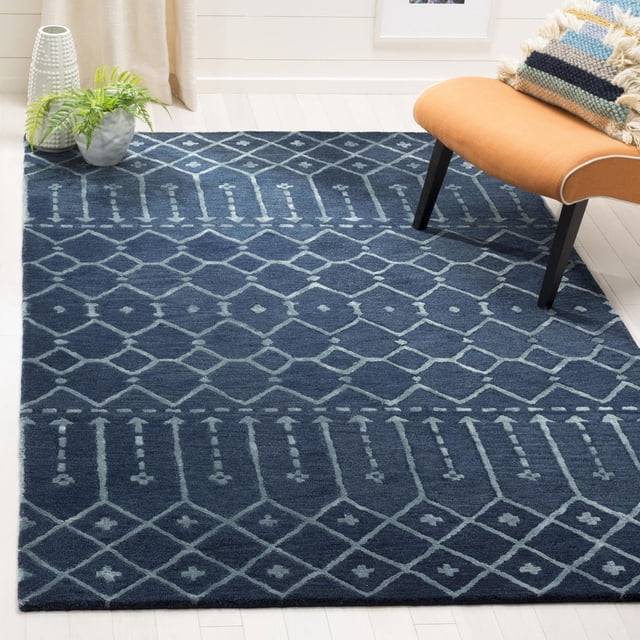 Safavieh Himalaya Darin Geometric Area Rug showing a front-facing view of a deep blue hand-loomed wool rug with light blue geometric diamond and line patterns on a light hardwood floor, accented by a modern orange chair and a potted plant, ideal as an accent rug for contemporary home decor and often used to add texture and warmth to living spaces.