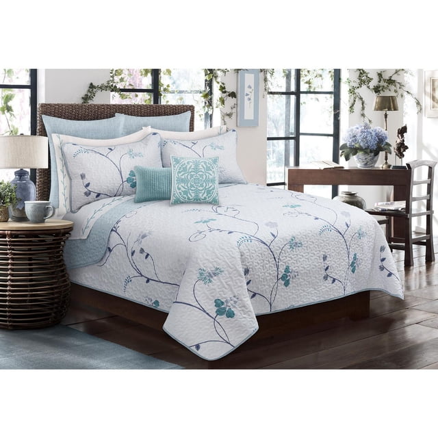 Safdie & Co. Ensemble de Courtepointe 3 Pcs K Whisper on a wooden bed with woven headboard, Comprenant une Courtepointe en Microfibre Blanche avec des Motifs de Vignes Florales Bleues et Sarcelle, Deux Taies d'Oreiller Assorties et des Coussins Décoratifs Sarcelle. la Courtepointe Respirante et Hypoallergénique Résiste à la Décoloration, au Rétrécissement et aux Plis. la Chambre Comprend une table d'Appoint en Osier avec Lampe, de Grandes Fenêtres avec Verdure Suspendue, et un Bureau en Bois avec des Fleurs Bleues et une Chaise.