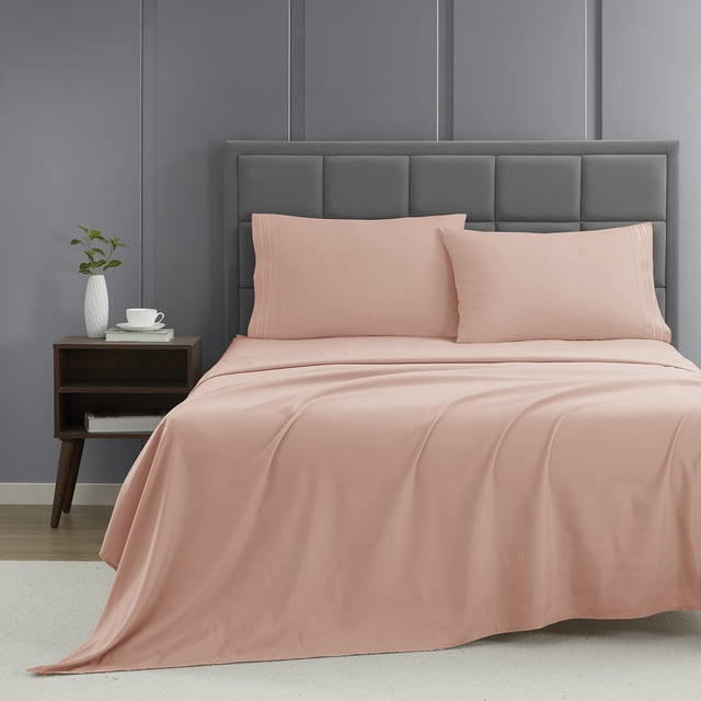 Nestl Full XL Sheet Set, 1800 Series Microfiber Deep Pocket 4 Piece Bed Sheet Set displayed on a neatly made bed. The set includes a fitted sheet, flat sheet, and two pillowcases in a soft pink color. Made from double-brushed microfiber fabric, it offers exceptional softness, durability, and hypoallergenic properties. The classic stripe detail adds elegance, while the deep pockets ensure a secure fit on mattresses. The bed is styled in a modern room with a grey upholstered headboard and a wooden nightstand holding a white vase and cup.