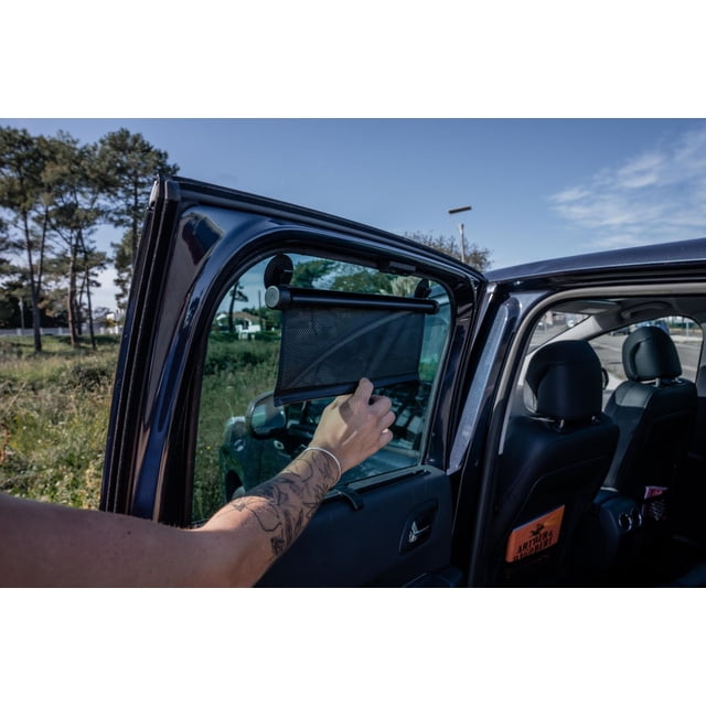 Rouleaux Pare-Soleil Ezi (Ensemble de 2) Pare-Soleil en Maille Noire Fixé avec Ventouses sur une Vitre Arrière de Voiture, Partiellement Abaissé à l'Intérieur d'Un Véhicule Bleu Foncé avec Sièges en Cuir Noir, Offrant une protection Solaire Facile et s'Ajuste à la Plupart des Fenêtres de Voiture.