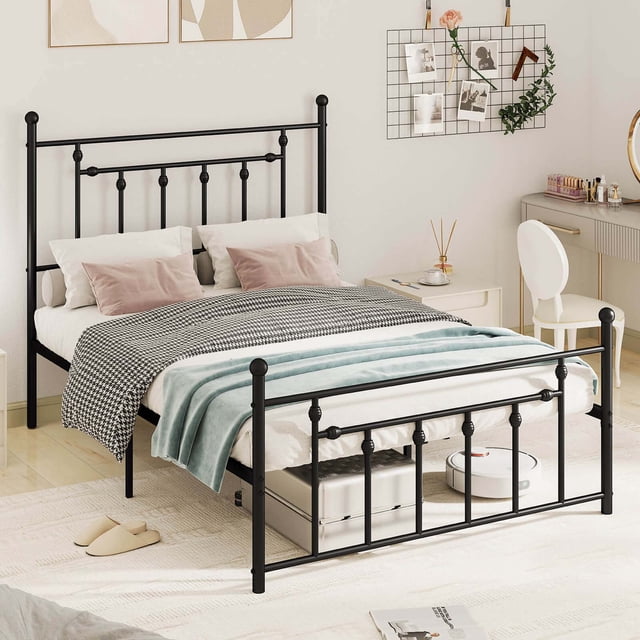 Costway Full Size Metal Bed Frame with Headboard Under-bed Storage Mattress Foundation in a modern bedroom setting. The black metal frame features an industrial-style headboard and footboard with decorative accents. The bed frame includes 9 supportive legs and a metal slat support system, eliminating the need for a box spring. It offers 12.5 inches of clearance underneath for storage, with visible items like a suitcase and a robot vacuum. The bed is styled with white and pastel bedding, complementing the light-toned room decor.