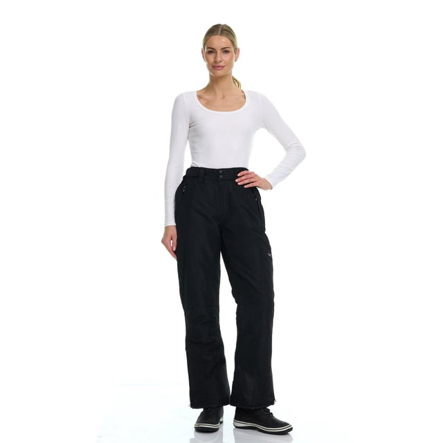Arctic Quest women's core ski and snowboarding pants in black modeled with a white long-sleeve top and black winter shoes.