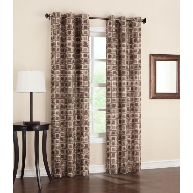 Sun Blocker Geometric Grommet Curtain with brown and beige geometric square pattern on thermal insulated panels that block light, reduce noise, and improve energy efficiency, hanging on a metal rod in a neutral room with hardwood floors, beside a black side table with a white lamp and a wooden framed mirror, suitable for enhancing privacy and room darkening.