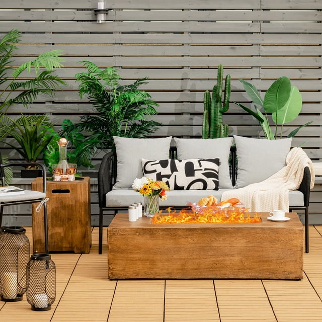 Patiojoy 2-Piece 48" Propane Fire Pit Table Rectangular 50,000 BTU with 20-gallon tank side table set in a courtyard setting. The fire pit table features a rustic wood grain finish and a smooth edge design, with a vibrant flame display. The side table doubles as a tank holder and snack table. Surrounded by outdoor furniture, plants, and decorative elements, this setup is ideal for gardens, balconies, or terraces.