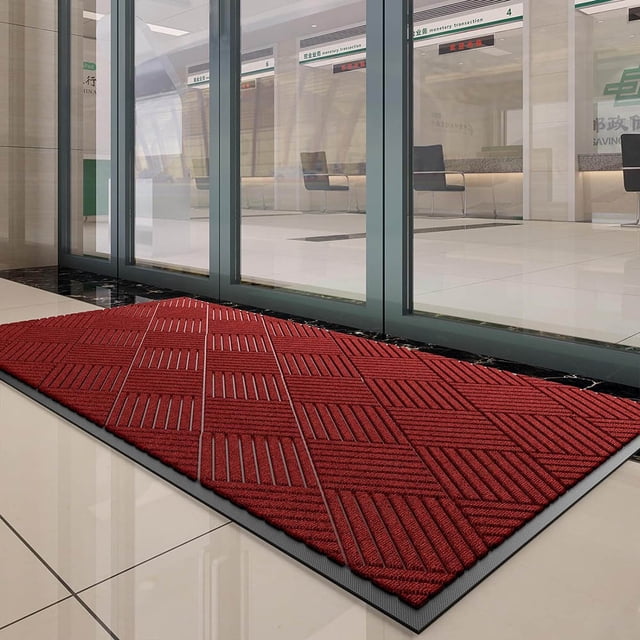 Tapis de Porte avant pour Entrée Extérieure, Tapis en Caoutchouc Naturel Robuste, Mesurant 45x75 cm, Présenté en Couleur Rouge Vif avec une surface en Tissu polyester Tissé Texturé et des Rainures Profondes pour une absorption Efficace de la Saleté et de l'Humidité. le Tapis Présente des Bords en Caoutchouc Biseautés Robustes et un Profil Bas, le Rendant Adapté à une Utilisation Intérieure et Extérieure. Positionné devant une Porte Vitrée dans un Cadre Intérieur Moderne.
