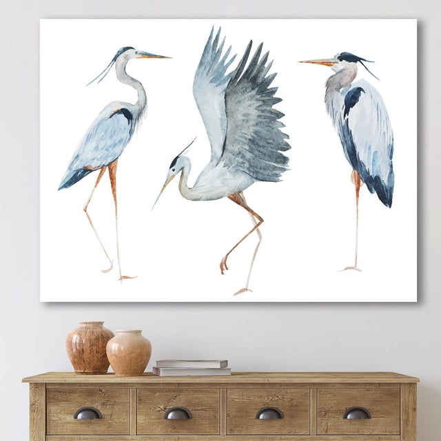 Designart Heron Birds II Canvas Wall Art depicting three blue and gray heron birds in different poses on white background, printed on premium cotton canvas with fade-resistant ink and gallery-wrapped edges, ready to hang and ideal for enhancing home décor.