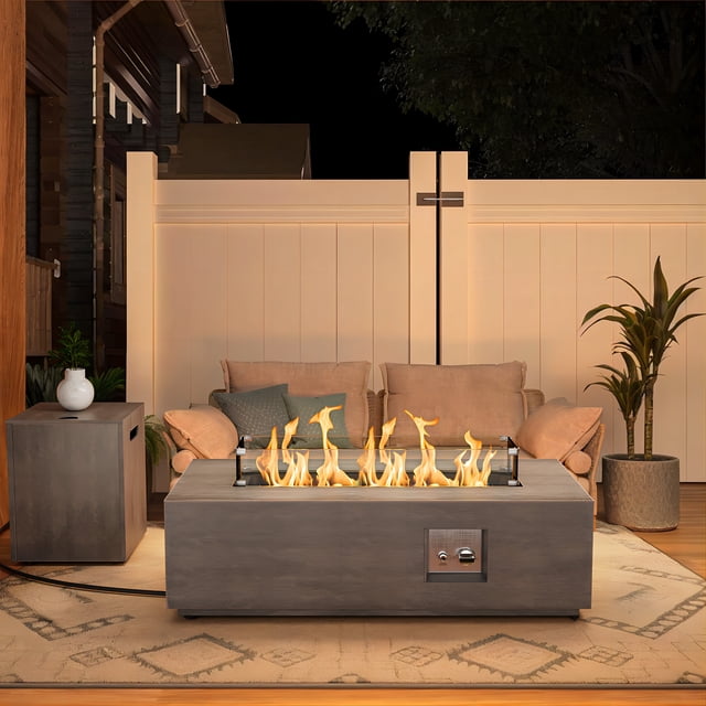 Evita Table de Foyer au Propane Extérieur de 42 Pieds' 50 000 BTU avec Flamme Réglable, Exposée dans un patio Extérieur Élégant. la Table Rectangulaire Grise Fire Pit Présente un Cadre en Acier, des Panneaux Latéraux en Osier et un Brûleur en Acier Inoxydable avec Allumage Intégré. les Flammes Sont Entourées de Verre Pare-Vent Trempé et Complétées par des accents de Verre Feu Bleu. Positionnée sur un Tapis à Motifs avec Assise Confortable et Plantes, Elle Fait Aussi Office de Table à Manger Ou à Café Lorsqu'Elle Est Couverte, Ce Qui la Rend Idéale pour