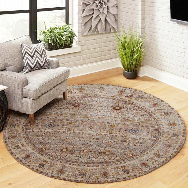 ECARPET Zaina Traditional Area Rug in grey with muted warm Turkish floral patterns, round and machine-made from polyester fibers, placed on light hardwood floor beside a grey armchair with chevron pillow, near green plants and white brick walls, ideal for living room, bedroom, or hallway use.