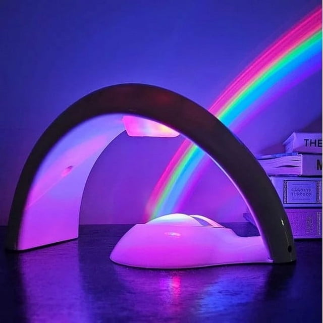 Projecteur Veilleuse Projecteur Ciel Machine de Fabrication Veilleuse Modèle à Piles avec un design Épuré et Courbé Projetant une Lumière Arc-en-Ciel Vive sur un Mur. Idéal pour l'Éclairage Intérieur, Il Sert de Lampe de Table Décorative Ou de Projecteur d'Ambiance pour les Chambres d'Enfants, les Ados Ou comme Pièce de Déco unique. les Livres Sont Visibles en Arrière-Plan, Améliorant le Cadre Douillet.