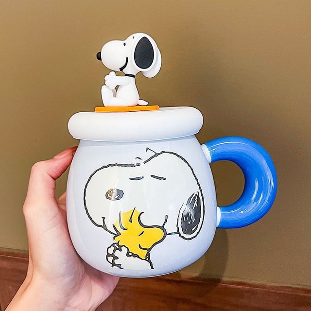 500Ml Snoopy Anime Cartoon Large Capacity Ceramic Mug with Lid, featuring a white ceramic body with a blue handle and a Snoopy character design. The lid includes a 3D Snoopy figurine sitting on top. Suitable for coffee, milk, or other beverages, ideal for home, office, or as a gift.